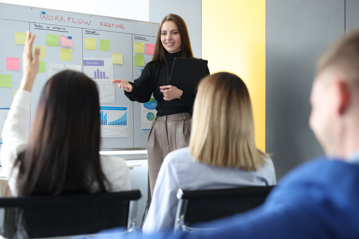 Woman business coach standing near blackboard and asking question to listener